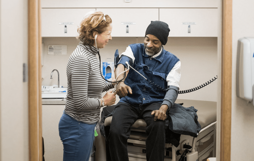 Female doctor taking the blood pressure of a homeless male patient